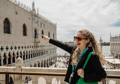 Tour guide pointing toward the Doge’s Palace from a terrace overlooking St. Mark’s Square in Venice.