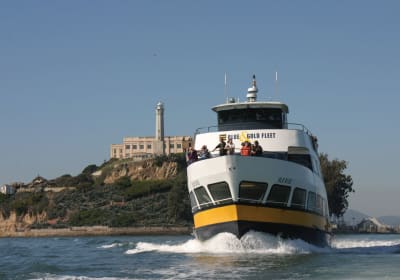 Blue and Gold Fleet ferry boat approaching Alcatraz Island with lighthouse visible on rocky shore