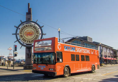Orange double-decker Skyline Sightseeing tour bus at Fishermans Wharf in San Francisco with iconic ship wheel sign