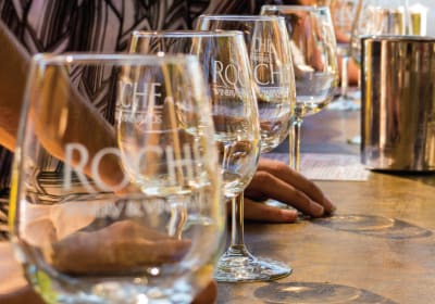 Wine tasting glasses with Roach Vineyard branding lined up on a wooden table during a vineyard tour