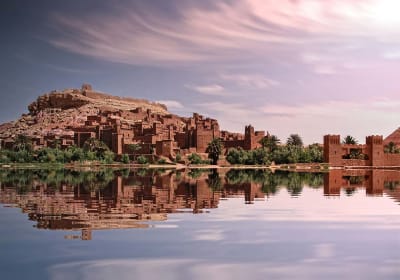 Ait Benhaddou Kasbah perfectly mirrored in the still water of an oasis, captured on a group 3-day desert tour from Marrakech to Merzouga.