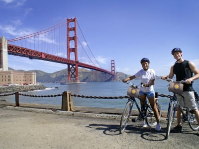 Three cyclists with bikes and helmets posing in front of the Golden Gate Bridge in San Francisco