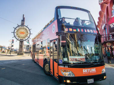 Red and orange double-decker tour bus at Fisherman's Wharf in San Francisco with iconic wheel sign visible