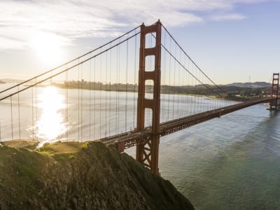 Golden Gate Bridge spanning San Francisco Bay with rocky coastline in foreground and city skyline visible in background