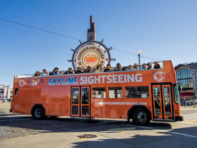 Orange double-decker Skyline Sightseeing tour bus with passengers on open-air upper deck near waterfront