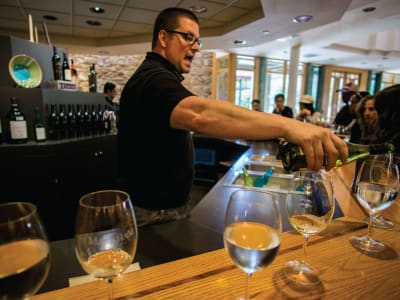 Wine tasting event with sommelier pouring white wine into glasses at a wooden bar counter