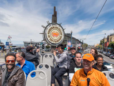 Tourists on a cable car at Fisherman's Wharf with the iconic ship's wheel sign visible in San Francisco