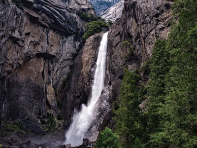 Tall waterfall cascading down rocky cliff surrounded by lush green vegetation in a mountain gorge
