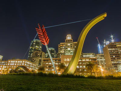Illuminated modern sculpture installations in urban park at night with city skyline backdrop