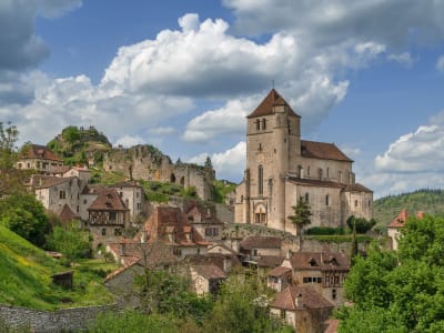 Panoramic shot of Saint‑Cirq‑Lapopie, showing the fortified church and red‑tiled stone houses on a green hillside in the Lot Valley of France.