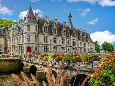 Elegant riverside building in Quimper with turrets and slate roofs, seen across a flower‑lined bridge over the river.