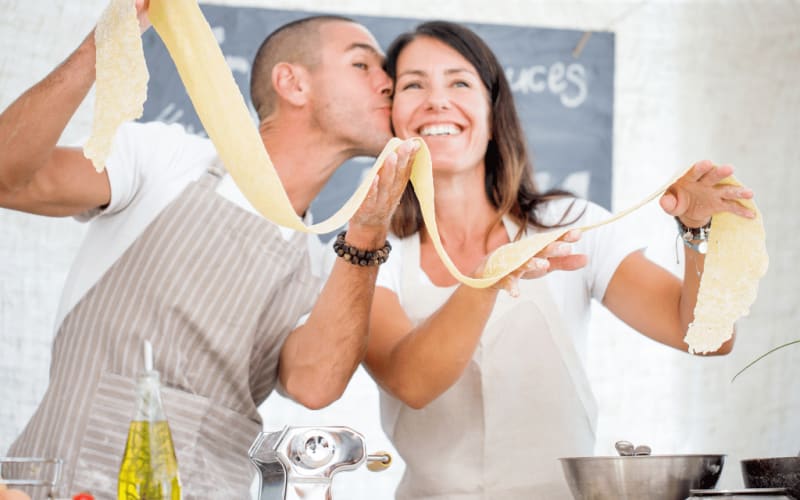 Couple happily stretching homemade pasta dough during an adult cooking class