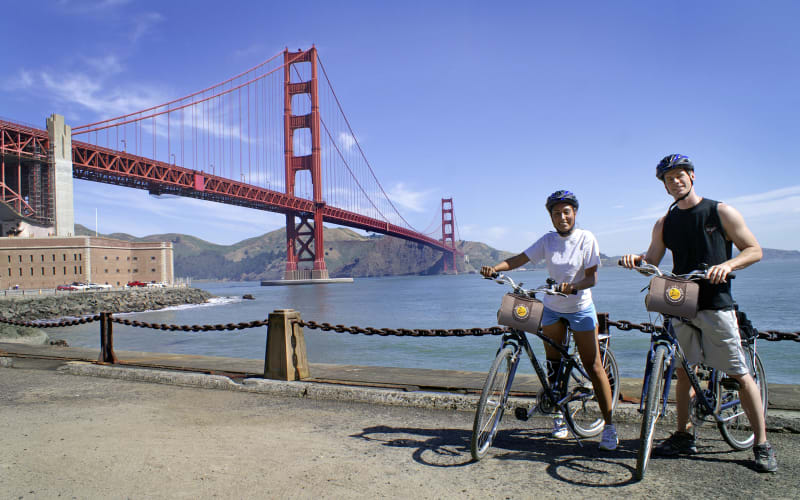 Three cyclists with helmets posing with bikes in front of the Golden Gate Bridge in San Francisco
