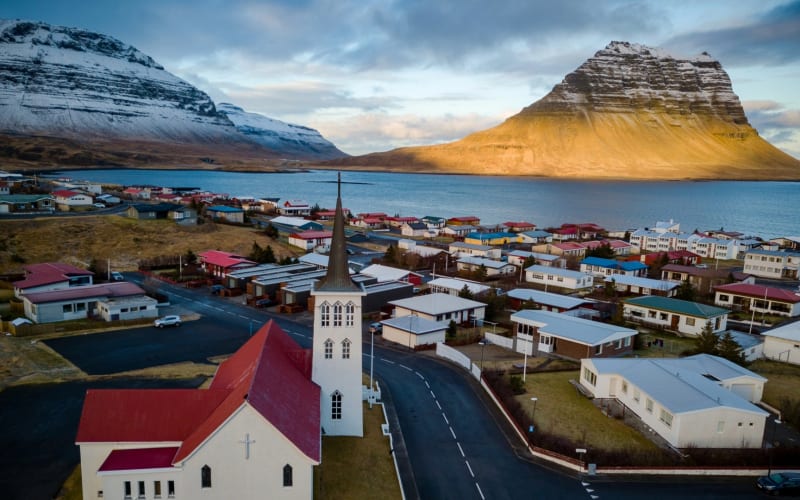 Aerial view of Grundarfjordur town at golden hour in winter, with colorful houses, a white church with red roof in the foreground, and Kirkj