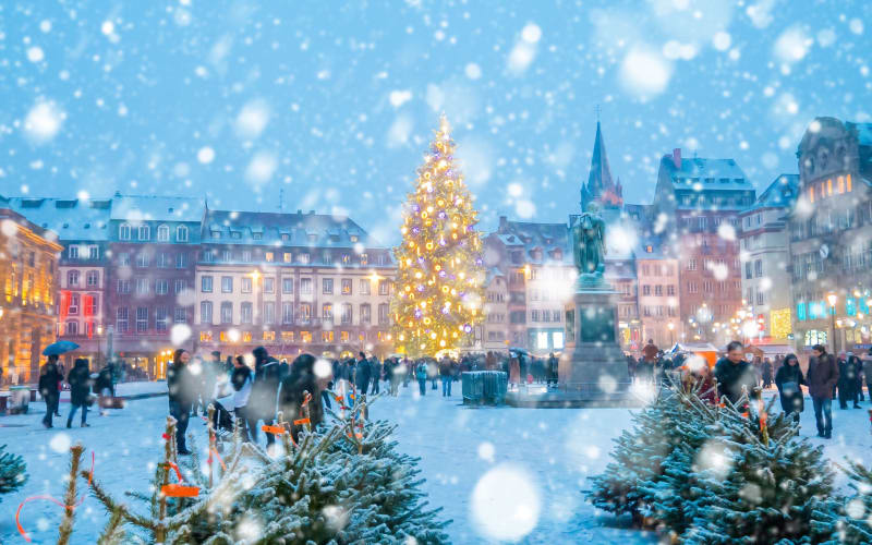 Guests walking through a Christmas market tour at dusk with festive lights, wooden chalets, and holiday decorations