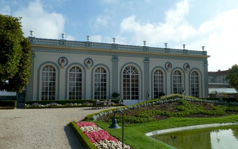 Moët & Chandon in Épernay, with tall arched windows, colorful flower beds, manicured lawns, and a reflecting pool.