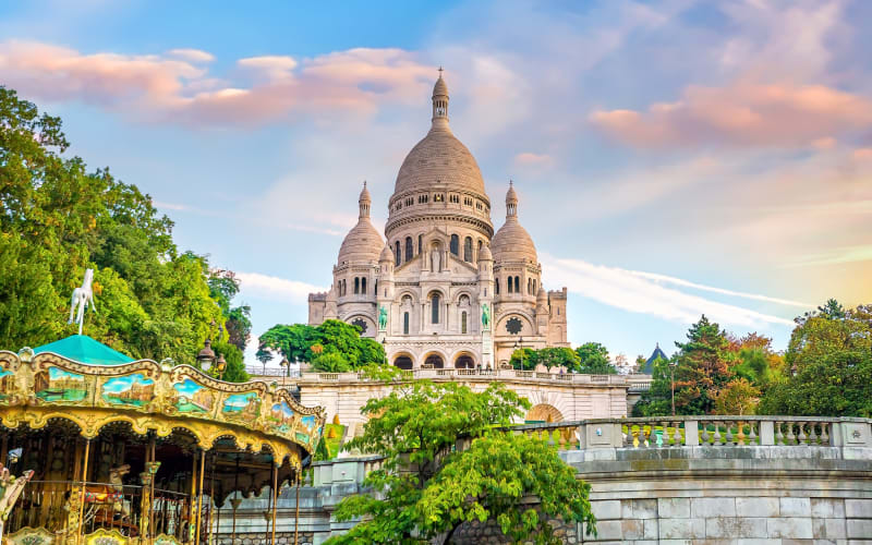 Sacré-Cœur Basilica rising above a traditional carousel in Montmartre, Paris, at sunset