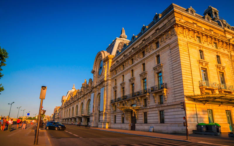 Musée d’Orsay’s stone façade and large exterior clock glowing in golden sunlight beneath a clear blue sky.