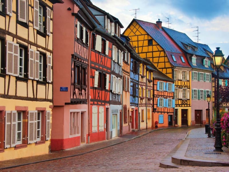  Row of colorful half-timbered houses along a cobblestone street in Colmar