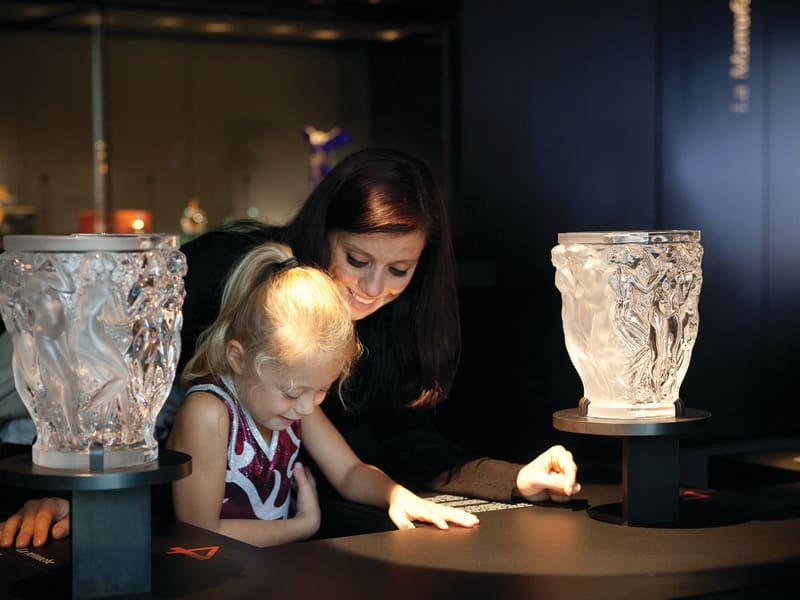 Mother and child explore illuminated Lalique crystal vases in the museum