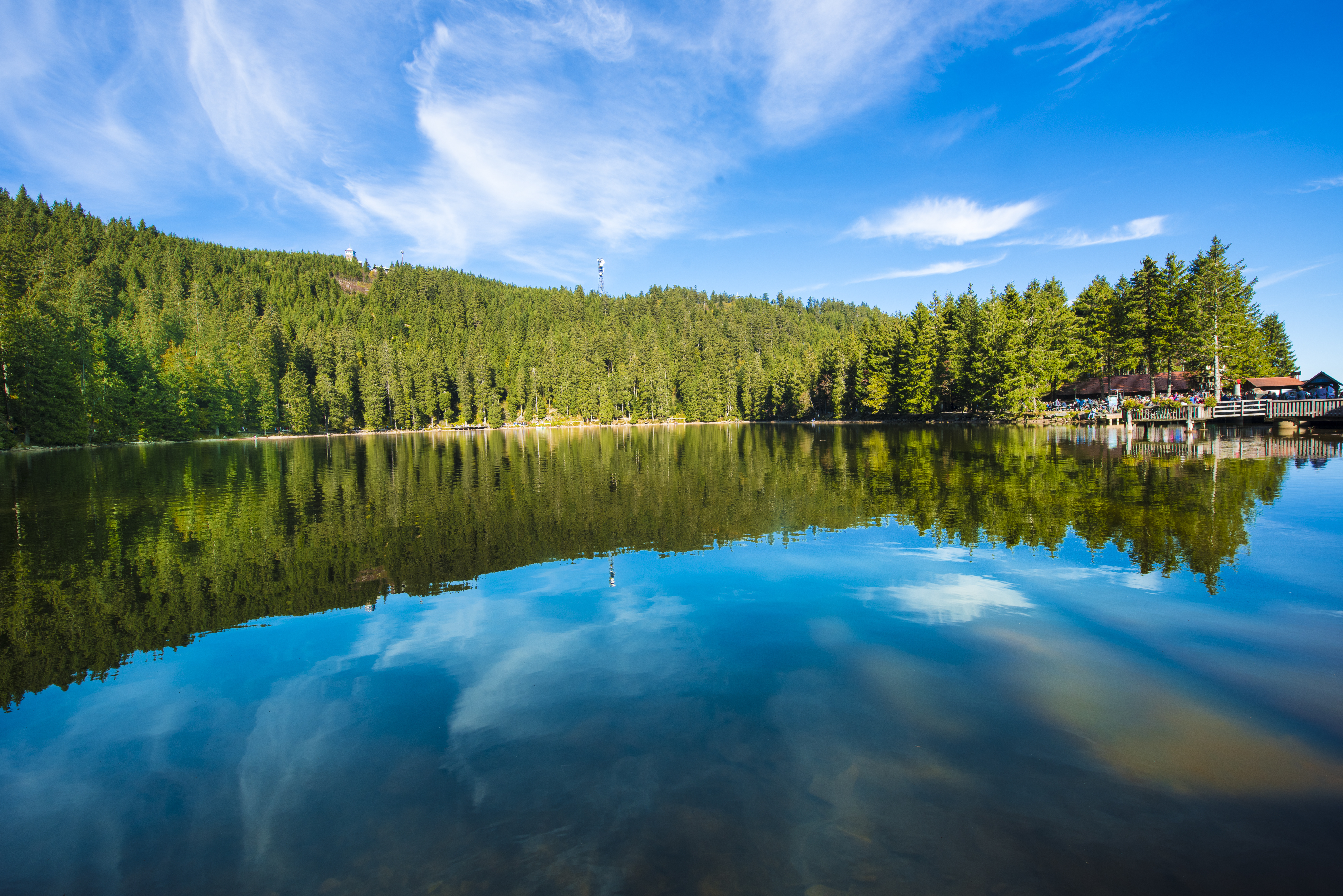 Still waters of Mummelsee reflecting pines and blue sky in the Black Forest