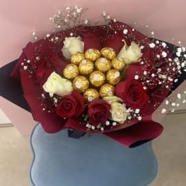 Red and White Roses with Baby's breath filling and Ferrero Rocher chocolate balls in the center wrapped in a red sheet tied with a black ribbon.