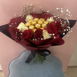 Red and White Roses with Baby's breath filling and Ferrero Rocher chocolate balls in the center wrapped in a red sheet tied with a black ribbon 