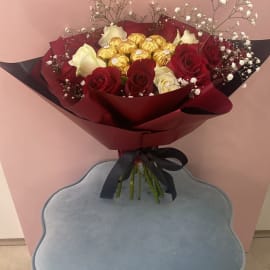 Red and White Roses with Baby's breath filling and Ferrero Rocher chocolate balls in the center wrapped in a red sheet tied with a black ribbon 