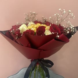 Red and White Roses with Baby's breath filling and Ferrero Rocher chocolate balls in the center wrapped in a red sheet tied with a black ribbon 