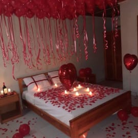  A romantic setting with 35 Red Helium Balloons, 3 Heart Shape Foil Balloons, Rose Petals, and Candles, creating an enchanting atmosphere.