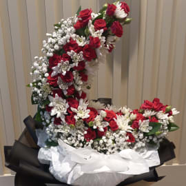 A stunning floral arrangement of red and white flowers in the shape of a crescent moon, perfect for a romantic gift or special occasion
