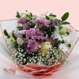 Bouquet wrapped in pink and white paper with golden trim, featuring yellow woolen sheep among fresh florals.