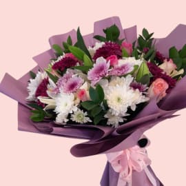 A vibrant, eye-level shot of the Floral Bliss Bouquet, emphasizing the arrangement of white and purple flowers, pink roses, and green foliage.