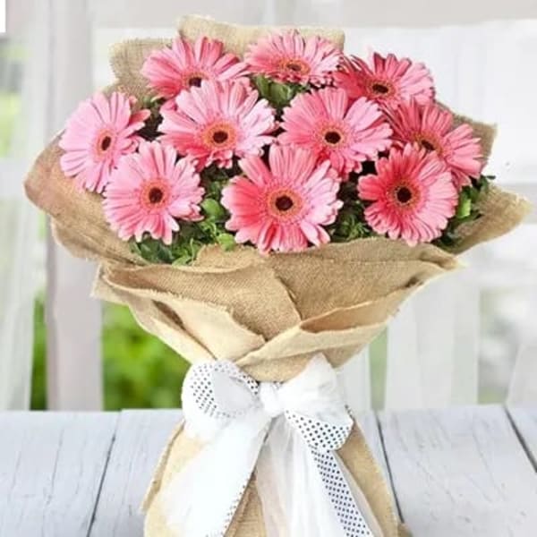 Pink gerbera bouquet in brown wrapping with white ribbon tied at the bottom 