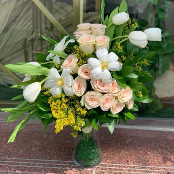 bouquet vase of Pink rose, white tulip, white gerbera, solidago and eucalyptus in a crystal-clear vase.