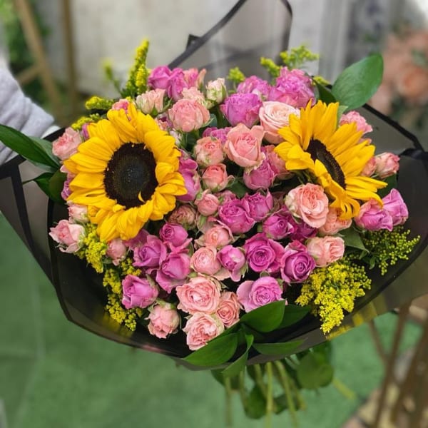Bouquet of Sunflowers, dark light pink roses, solidago and eucalyptus in black wrapping. 