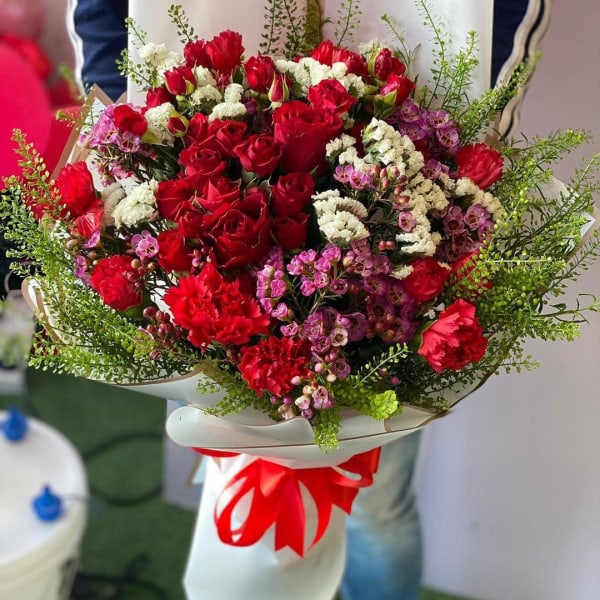 Bouquet of  red roses with red carnation and solidago in an elegant white wrapping.