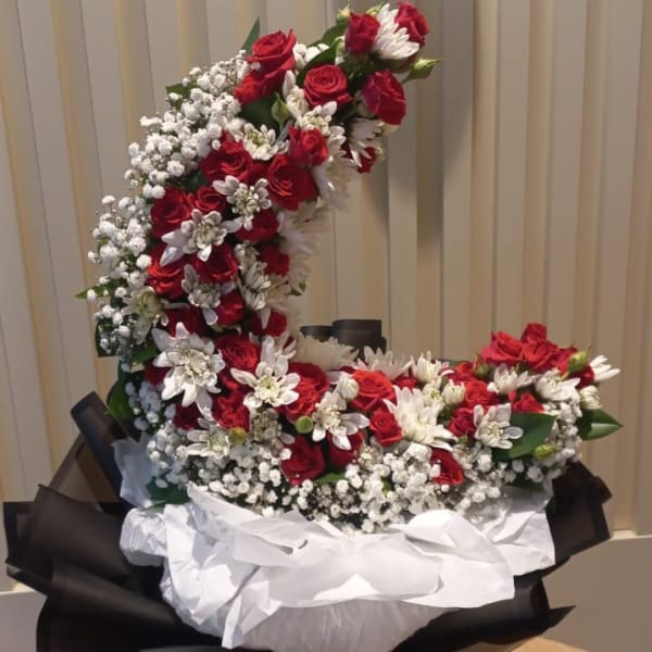 A moon-shaped bouquet of red roses and white chrysanthemums, wrapped in black and white paper and resting on a wooden table.