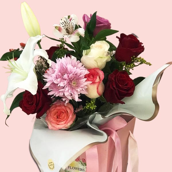 In a lovely pink box, red and pink roses with white lily, alstroemeria, chrysanthemum, and solidago.