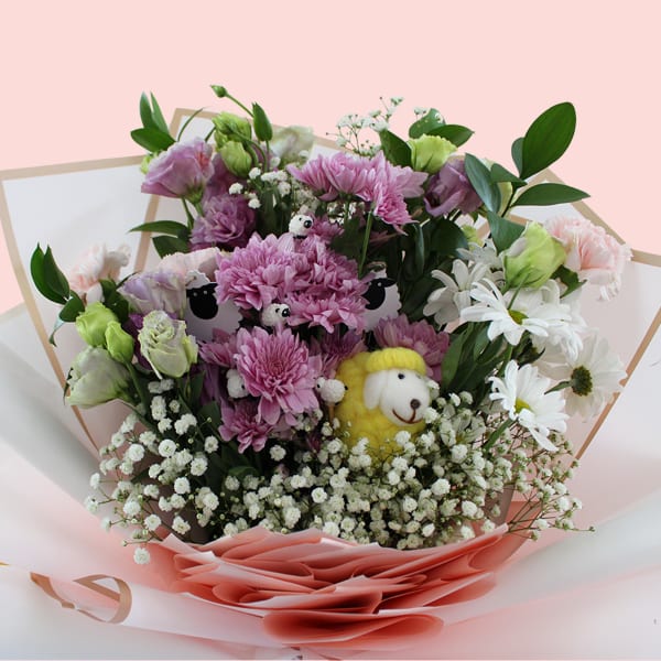 Bouquet wrapped in pink and white paper with golden trim, featuring yellow woolen sheep among fresh florals.