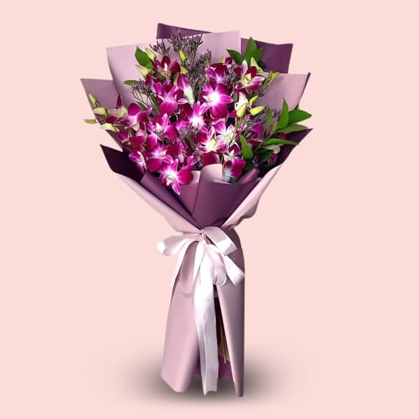 A close-up of a bouquet of purple orchids wrapped in pink and purple paper, tied with a white ribbon. The orchids are the main focus, with hints of green leaves and small purple filler flowers visible