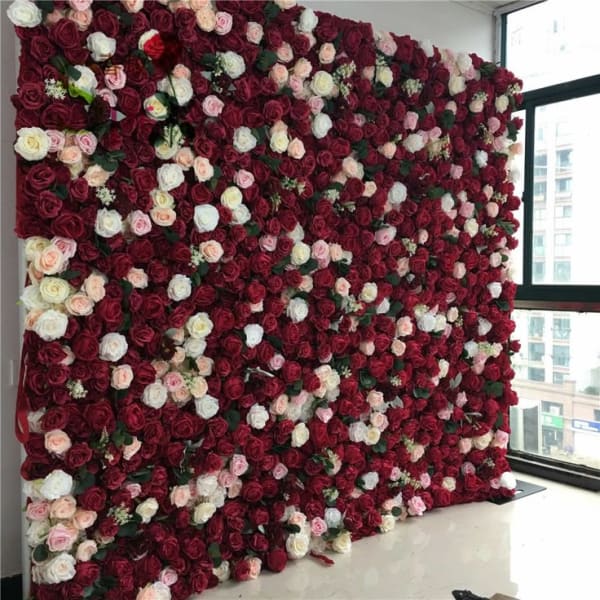 A large, full-coverage wall of artificial flowers in shades of dark red, light pink, and white, creating a dense, textured backdrop for an event