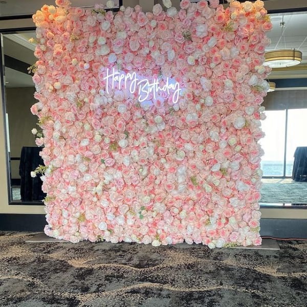A large, full-coverage wall of artificial flowers in shades of dark red, light pink, and white, creating a dense, textured backdrop for an event.