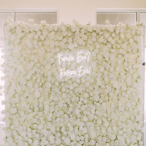 White rose floral wall with a neon sign that says 