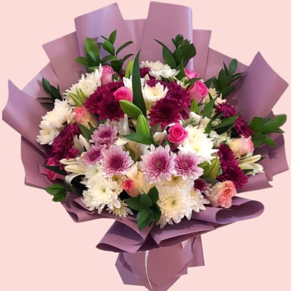 A close-up shot of the Floral Bliss Bouquet, showcasing a beautiful mix of white lilies, white and purple chrysanthemums, and pink roses wrapped in purple paper.