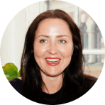 smiling woman with long black hair and natural makeup, bright indoor setting with plants and soft natural light