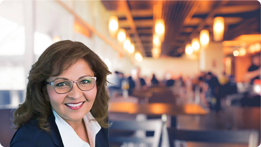 Smiling woman with glasses in an inviting café setting, featuring warm lighting and a bustling background. woman, café