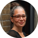 woman with glasses smiling against a brick background, middle-aged woman with a bun hairstyle and round glasses