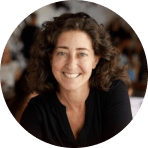 portrait of a smiling woman with curly hair, casual setting with blurred background elements