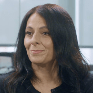 portrait of a woman with long black hair, wearing a black top, smiling in an office environment, professional woman in an office setting